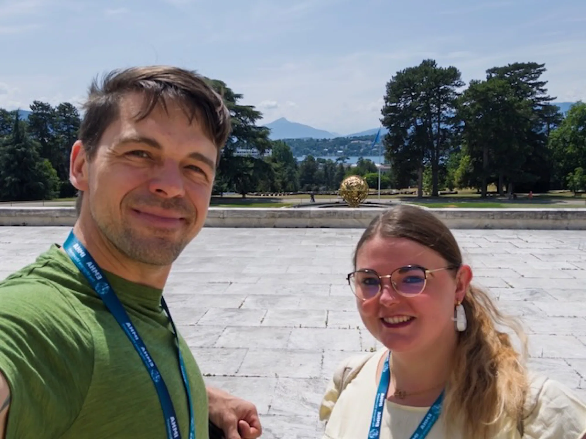 Stefan Kohlweg und Tamara vor dem Palais des Nations in Genf, im Hintergrund die Kugel-Skulptur und der Genfersee.